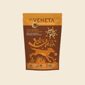 A stand-up pouch of Dr. Veneta Stay Mobile dog food, featuring a brown and golden-yellow design with an illustration of a running dog and a bone, set against a solid cream background.