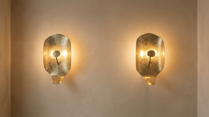 Two gold wall sconces on a beige wall